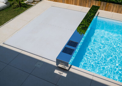 Piscine moderne recouverte d’une couverture Coverseal beige, avec habillage effet miroir équipé de panneaux solaires, intégrée dans une terrasse carrelée.