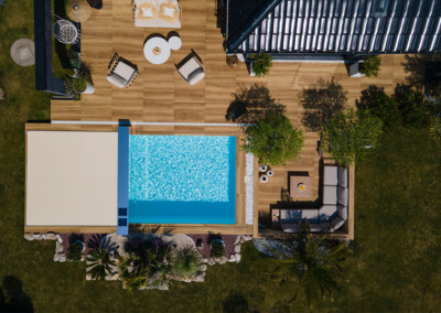 Vue aérienne d’une piscine haut de gamme équipée d’une couverture Coverseal beige, intégrée dans une terrasse design avec salon de jardin moderne.