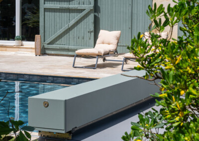Gros plan sur l'habillage de la Coverseal grise au bord de la piscine, avec en arrière-plan les transats et la maison en pierre.