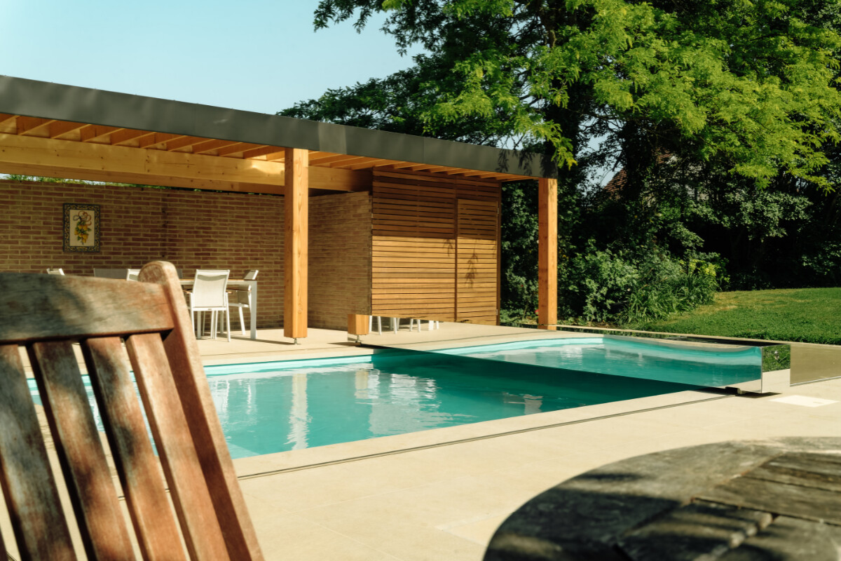 Gros plan sur l'habillage de la Coverseal grise au bord de la piscine, avec en arrière-plan les transats et la maison en pierre.